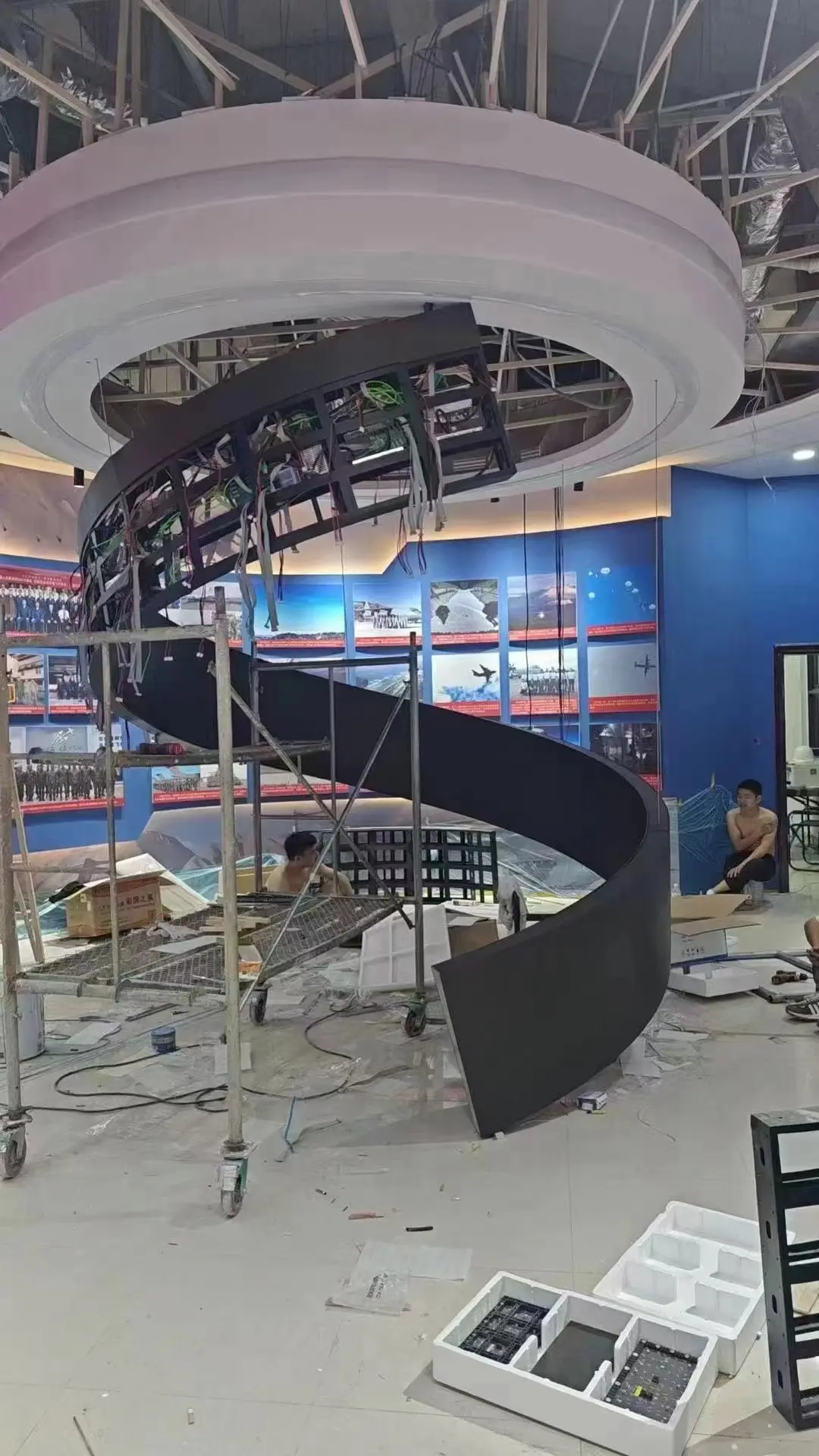 Flexible LED modules partially installed on a spiral frame with exposed wiring in an exhibition hall